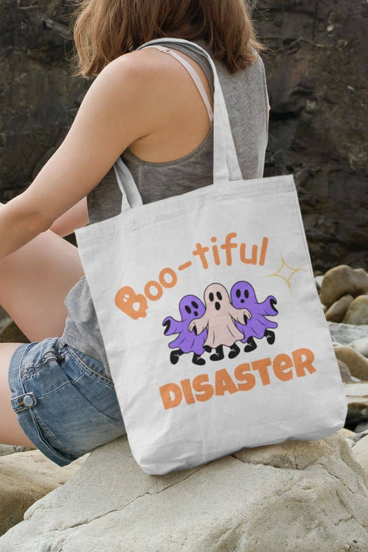 Spooky tote bag with a girl holding a tote bag with 'Boo-tiful Disaster' design on a rocky surface