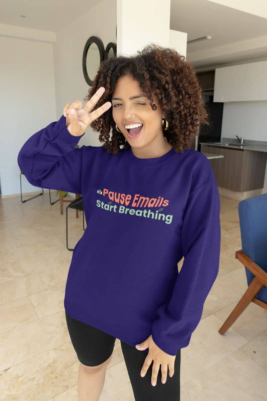 Stress relief sweatshirt with a person wearing a purple sweatshirt with text "Pause emails, Start Breathing" in a modern indoor setting