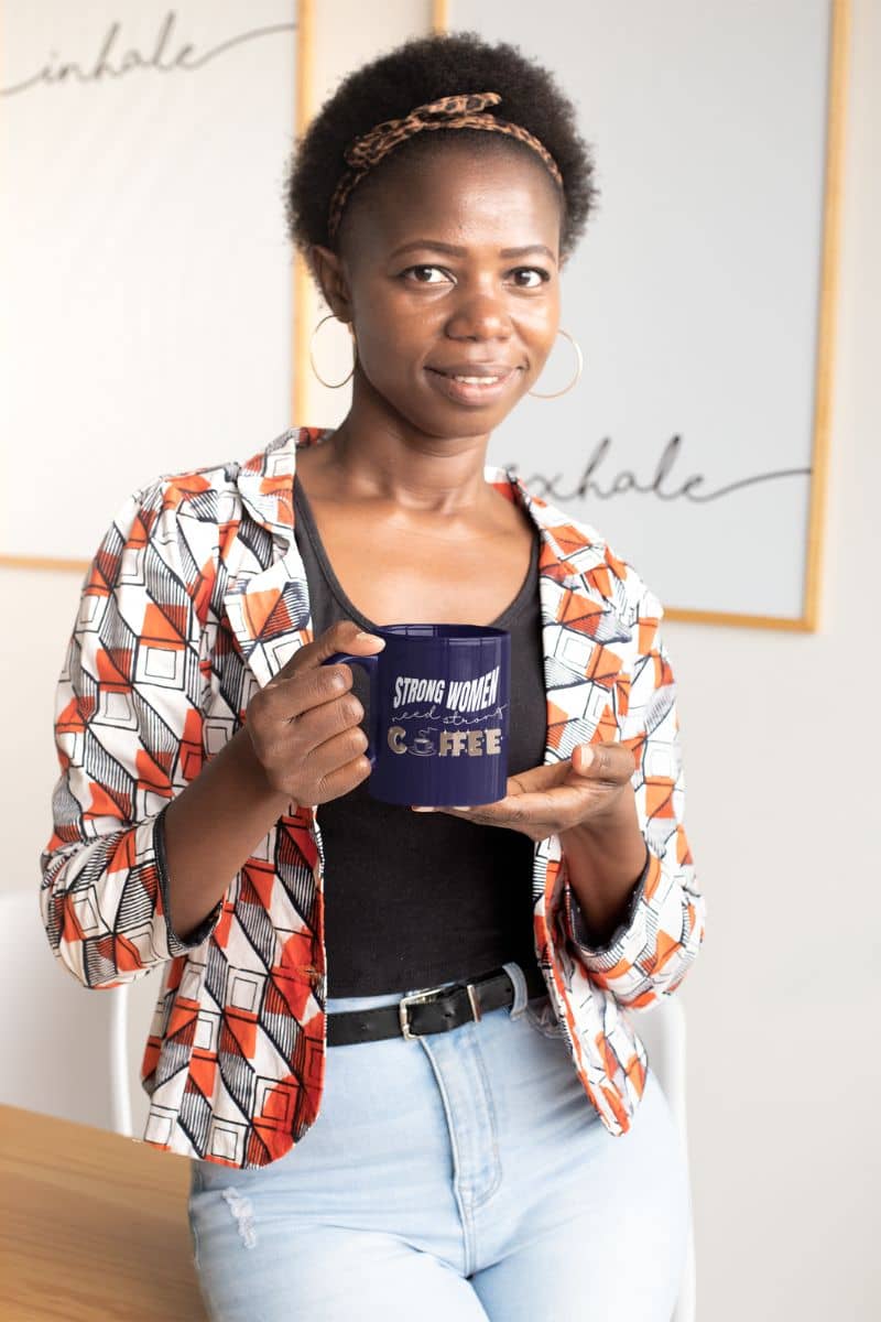 Strong women need strong coffee mug with a girl holding a cup of coffee standing in front of the presentation board with a slight smile