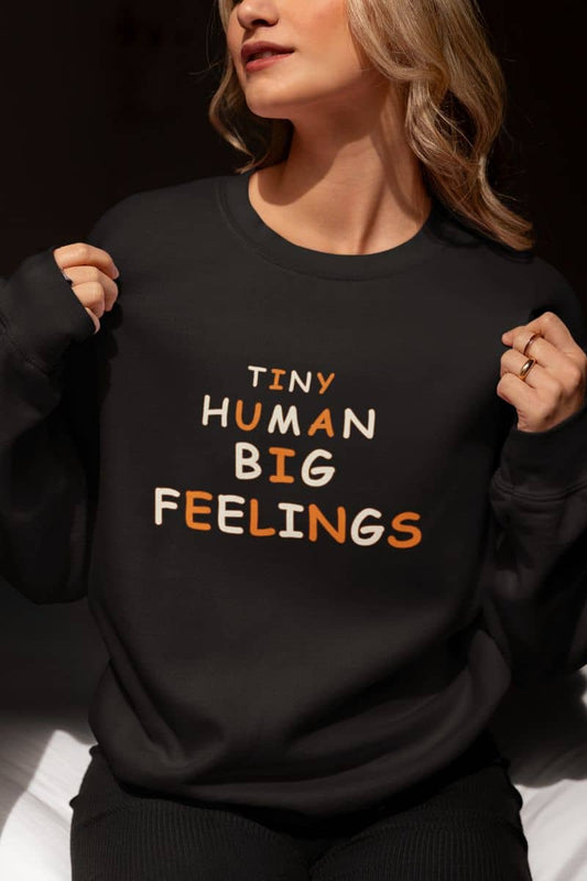 Teacher sweater with a woman wearing a black crewneck sweatshirt with text 'Tiny Human Big Feelings' 