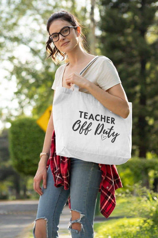 Teacher work bag with a woman outdoors carrying a white canvas tote bag printed with the words 'TEACHER Off Duty' in black lettering. 