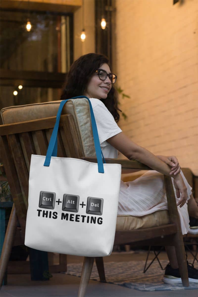 Tote bag office with a woman sitting on a chair with a tote bag featuring keyboard keys design and text 'Ctrl + Alt + Del This Meeting'