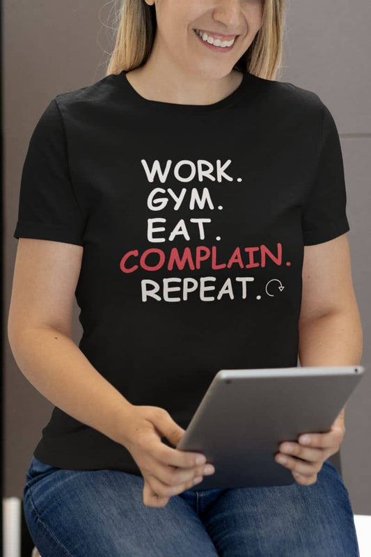 Trendy graphic t-shirt with a girl in a black t-shirt with text 'Work. Gym. Eat. Complain. Repeat' and holding a tablet.