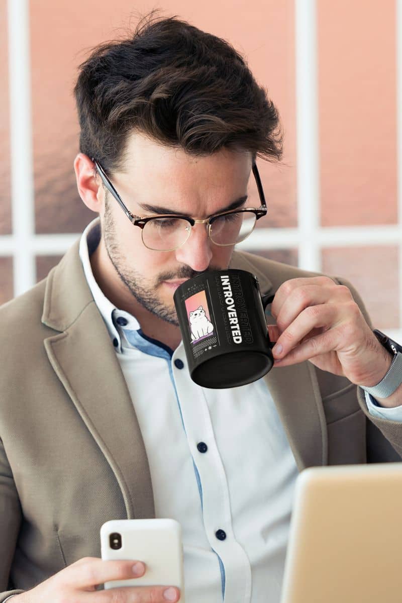 Unique introverted coffee mug with a man wearing a suit while holding a cup of water in one hand and a phone in the other hand while working on a laptop