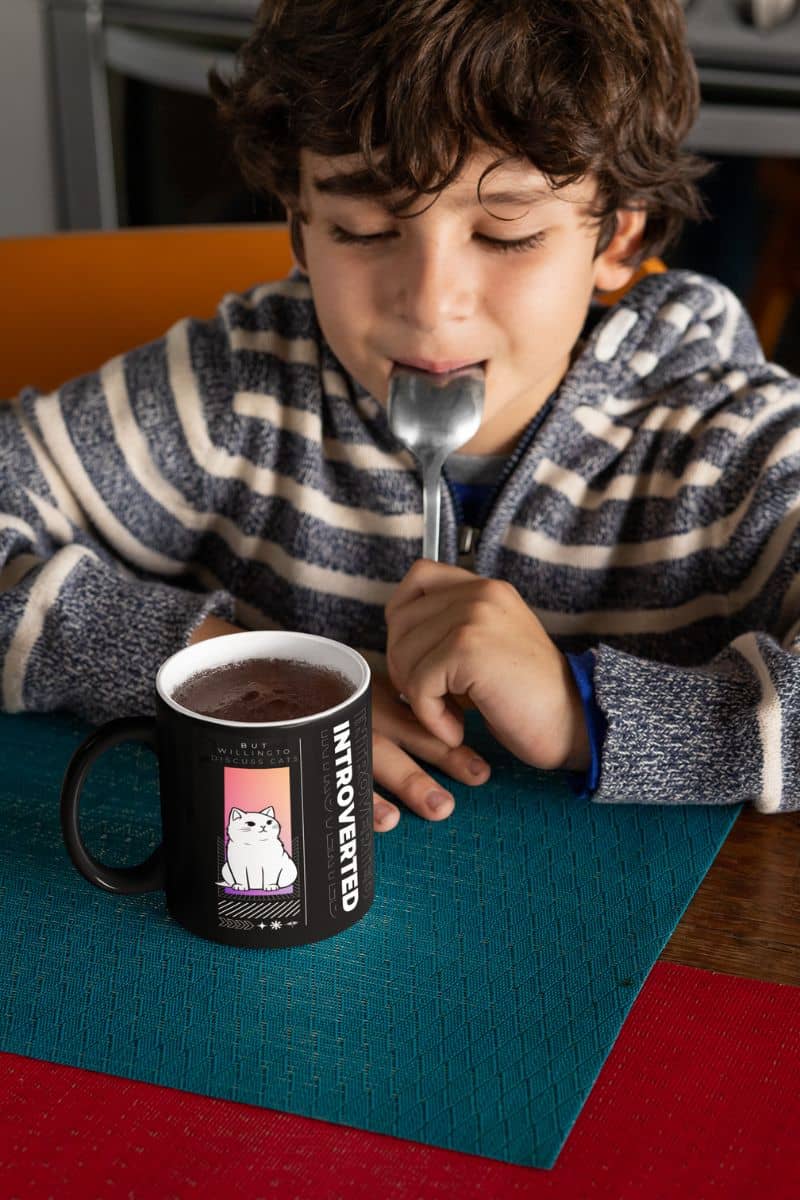 Unique introverted coffee mug with a boy holding a spoon in his mouth and looking at a cup of cocoa on the dining table