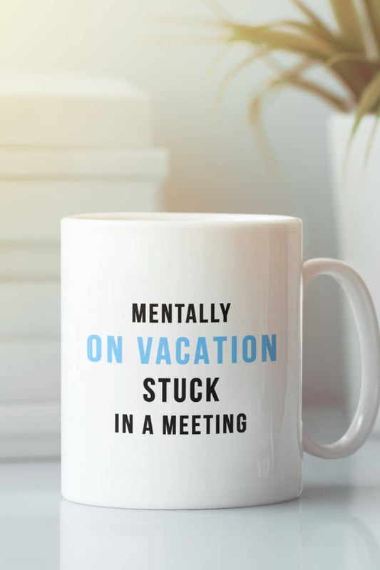 Vacation coffee mug featuring a white mug with text 'Mentally on vacation stuck in a meeting' on a blurred background