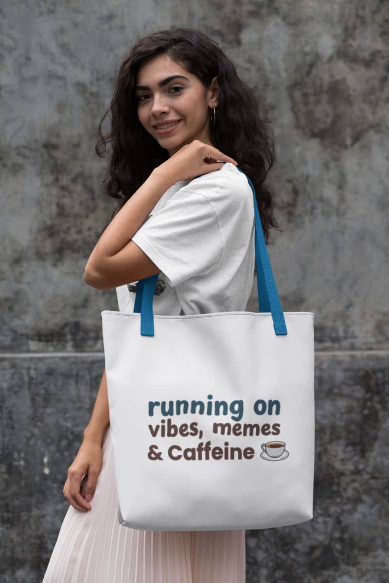Vibe check tote with a woman holding a tote bag with text 'running on vibes, memes & caffeine' against a stone wall.