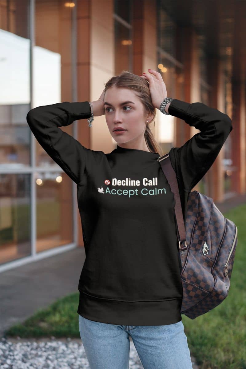 Wellness affirmation sweatshirt with a woman wearing a black sweatshirt with text 'Decline Call, Accept Calm', standing outdoors.