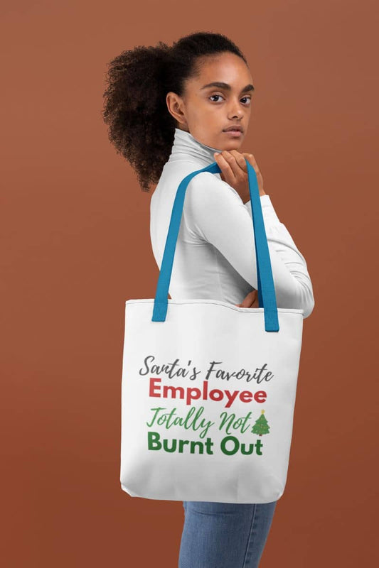 Witty office tote bag featuring a person holding a tote bag with text 'Santa's Favorite Employee Totally Not Burnt Out' against a brown background