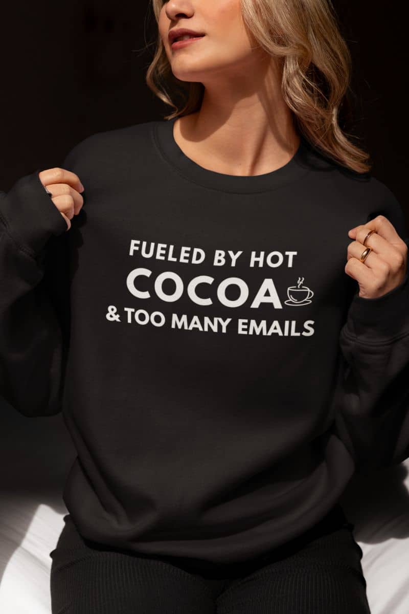 Work from home sweatshirt with a person wearing a black sweatshirt with text 'Fueled by hot cocoa & too many emails'.