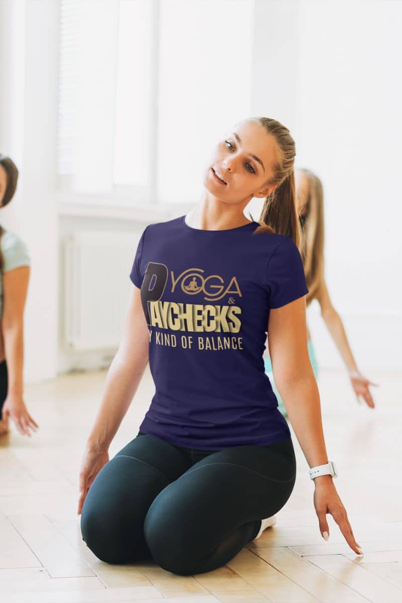 Work life balance t-shirt with a woman in a yoga pose wearing a purple t-shirt with text 'Yoga & Paychecks – My Kind of Balance' in a bright indoor setting