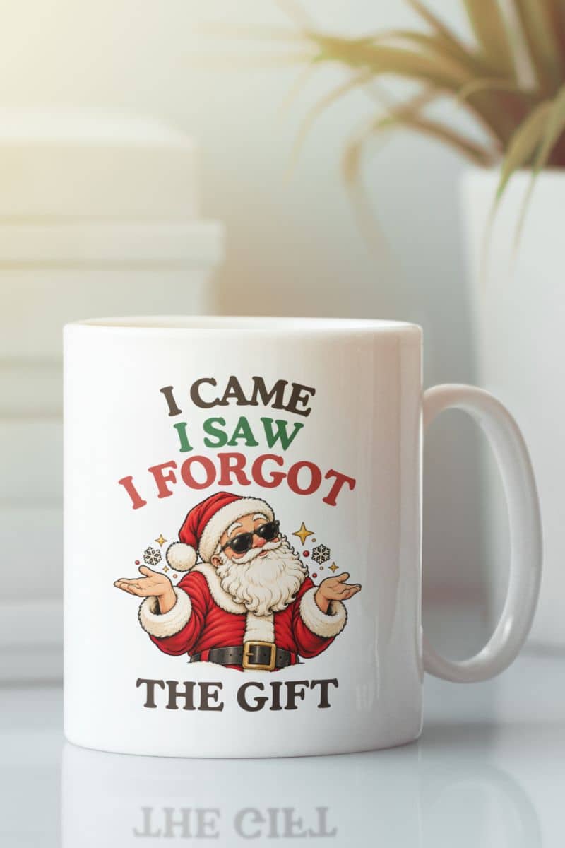 Xmas coffee mugs – White ceramic mug on a tabletop featuring a shrugging Santa in sunglasses and the funny “I Came. I Saw. I Forgot the Gift” design.