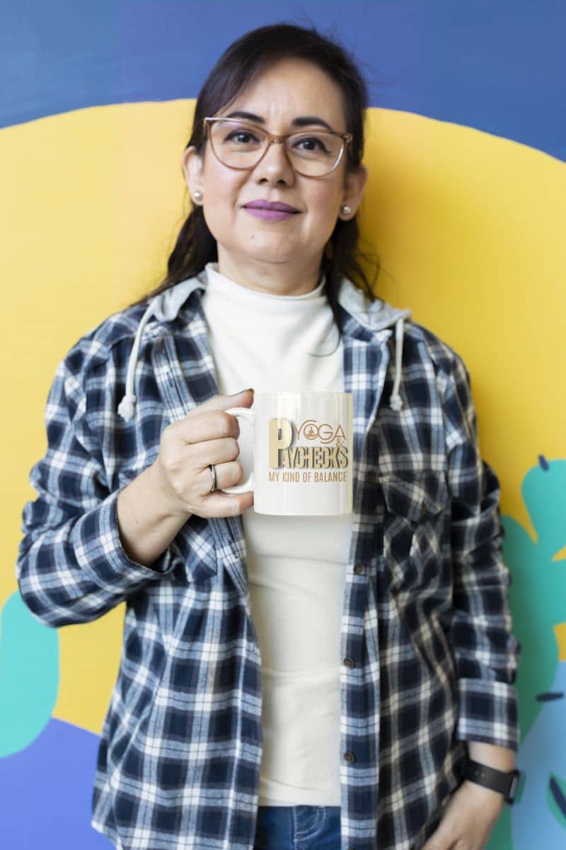 Yoga and paychecks mug with a middle aged woman holding a cup of coffee posing