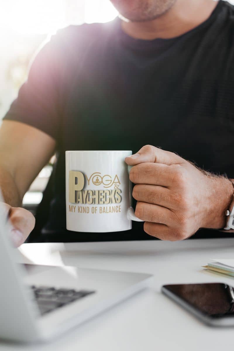 Yoga and paychecks mug with a man working on a laptop while holding a cup of coffee in his hand