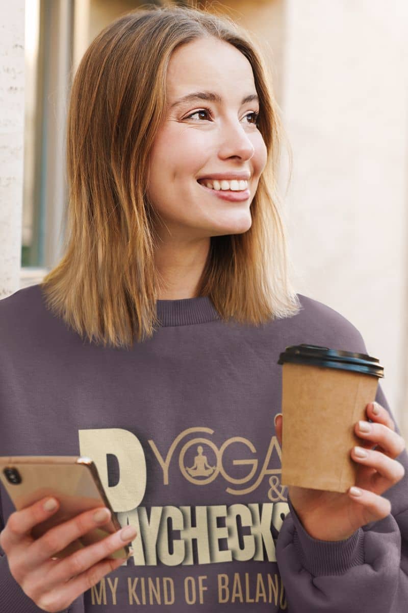 Yoga and paychecks sweatshirt with a girl smiling brightly while holding a cup of coffee and a phone in both hands