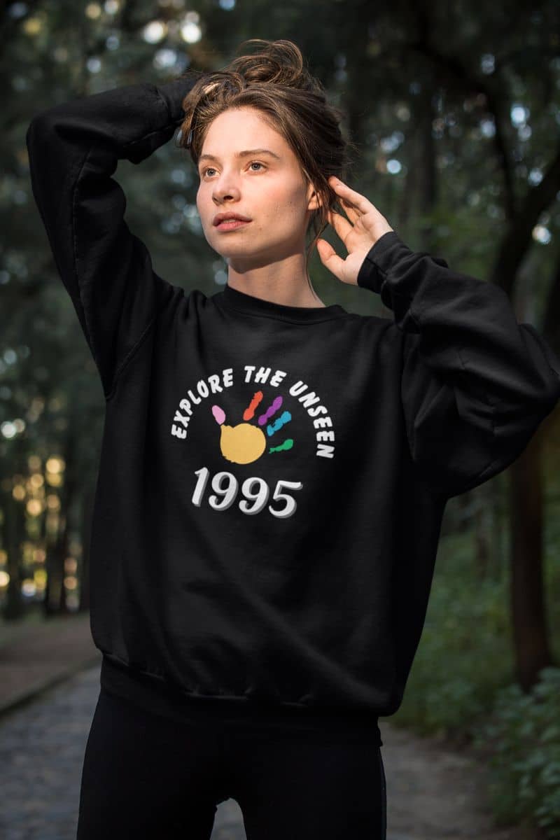 adventure lifestyle sweatshirt with a person wearing a black sweatshirt with 'Explore the Unseen 1995' design in a forest setting
