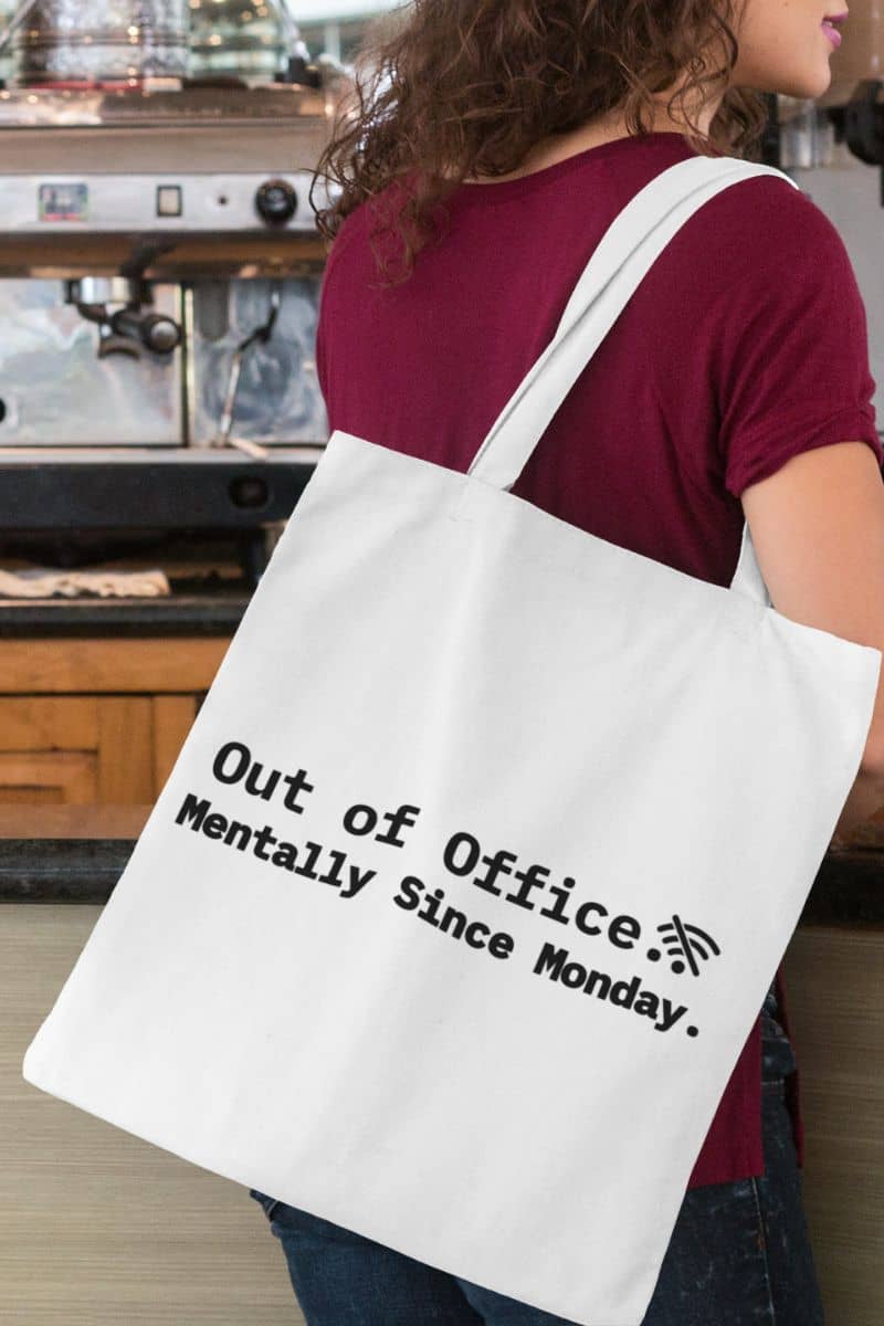 anti work quote tote with a person wearing a white tote bag with text 'Out of Office. Mentally Since Monday' in a coffee shop setting