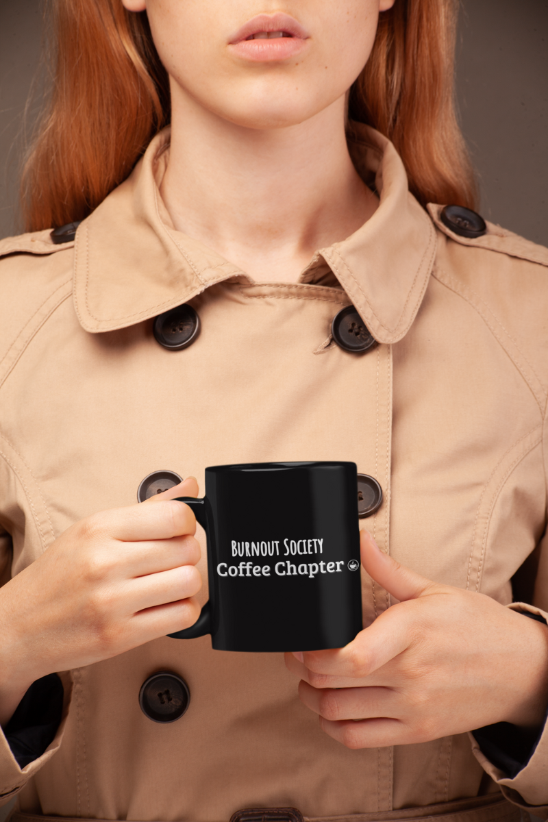 anxious office coffee cup with a person holding a black mug with 'Burnout Society Coffee Chapter' text, wearing a beige trench coat.