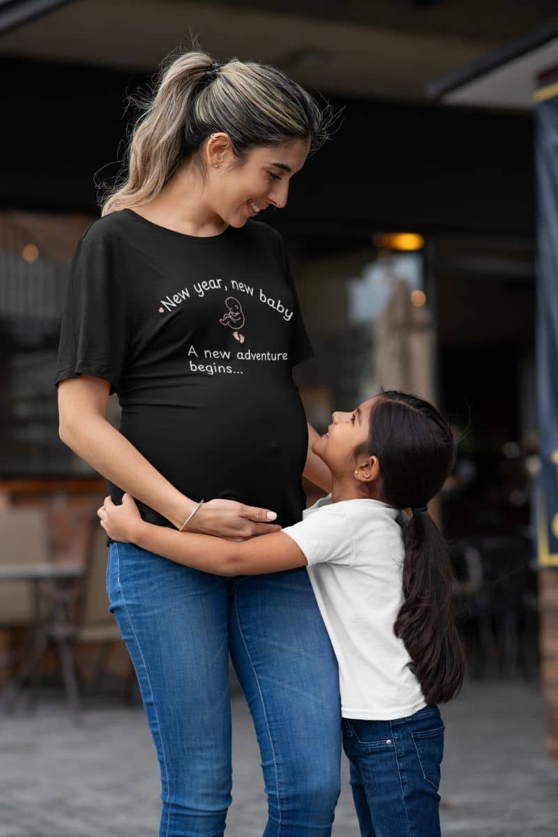 Baby announcement shirt featuring a pregnant woman wearing a black t-shirt with the words “New Year, New Baby. A new adventure begins…” while talking to her daughter