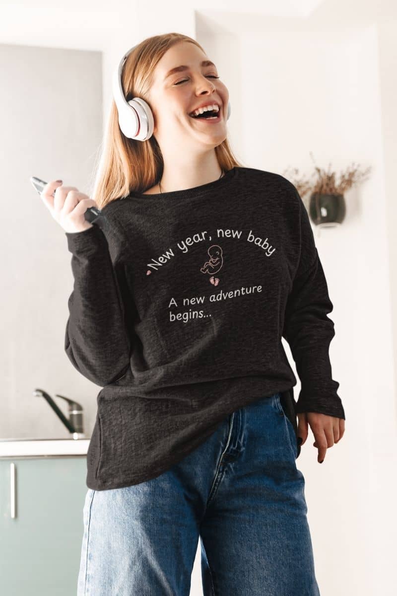 baby announcement sweatshirt with a girl wearing a black sweatshirt featuring  the text 'New year, new baby. A new adventure begins...'