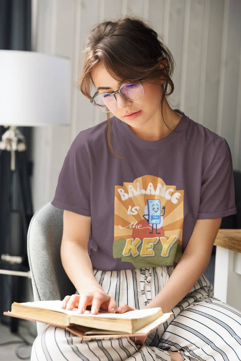 balance quote tee with a woman wearing a t-shirt with 'Balance is the Key' graphic reading a book indoors.
