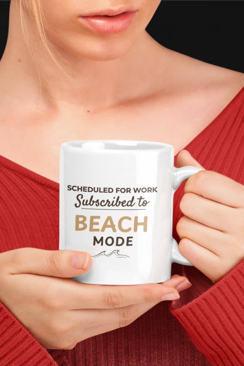beach coffee mug with a person holding a white mug with text 'Scheduled for work, subscribed to beach mode' against a black background.