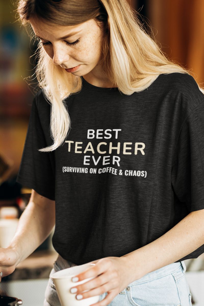 best teacher t-shirt with a person wearing a black t-shirt with 'Best Teacher Ever. (Surviving on coffee & chaos)' text, holding a cup.