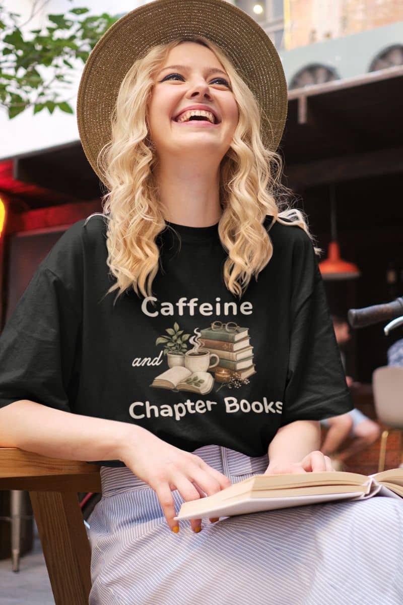 book lover t shirt with a woman wearing a black t-shirt featuring the text 'Caffeine and Chapter Books', sitting at the coffee shop.
