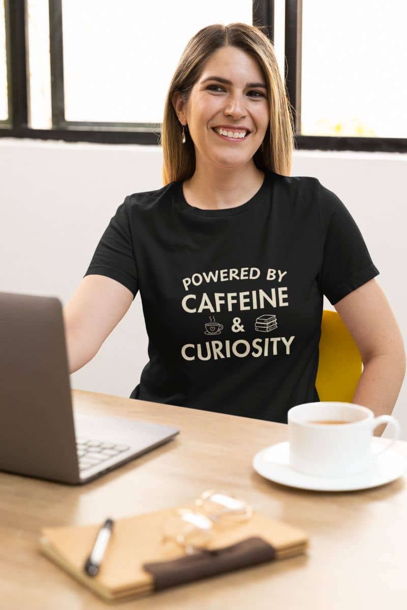 book lover tee with a woman wearing a black t-shirt featuring the text 'Powered by Caffeine & Curiosity'