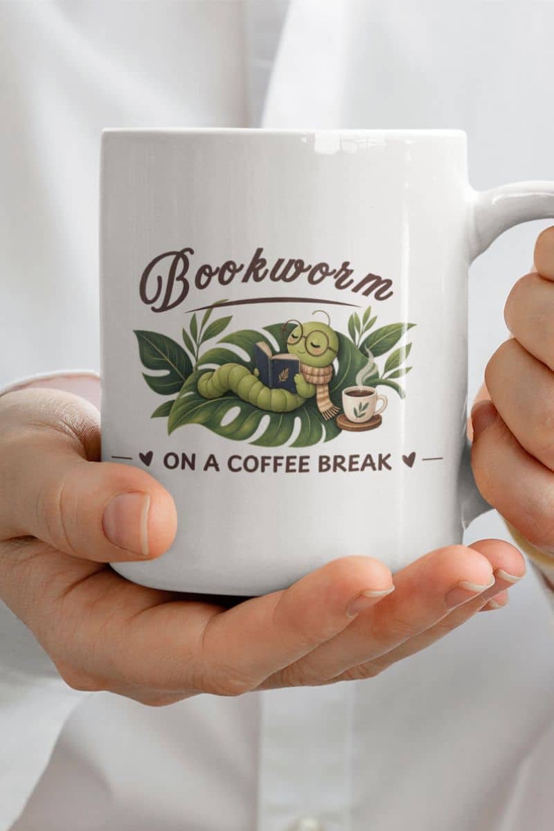 A bookworm mug featuring the text 'Bookworm on a Coffee Break', held in two hands against a white shirt background.
