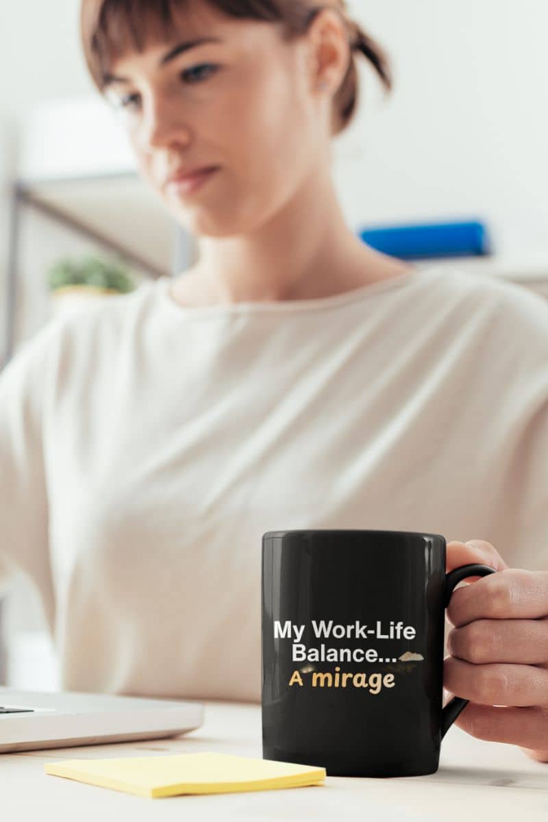 boss employee humor mug with a person holding a black mug with 'My Work-Life Balance... A Mirage' text in an office setting.