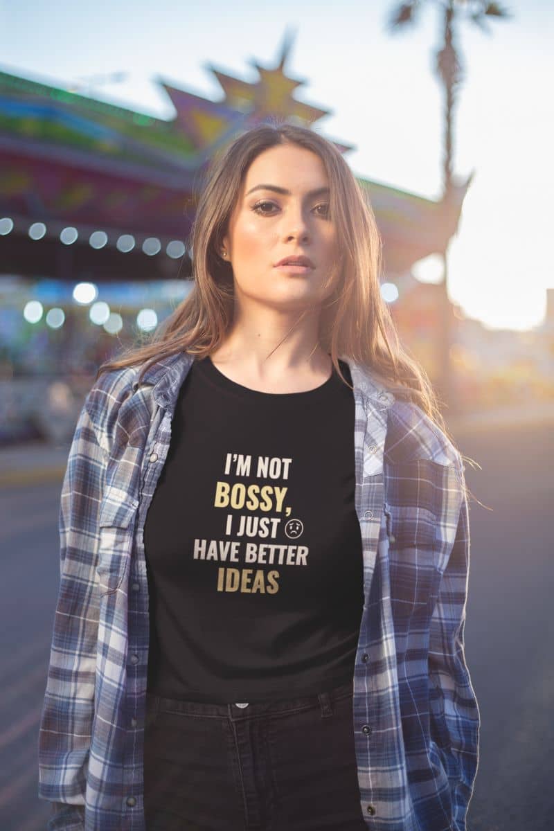 bossy quote shirt with a woman wearing a black t-shirt with text 'I’m Not Bossy, I Just Have Better Ideas' in a plaid shirt outdoors.