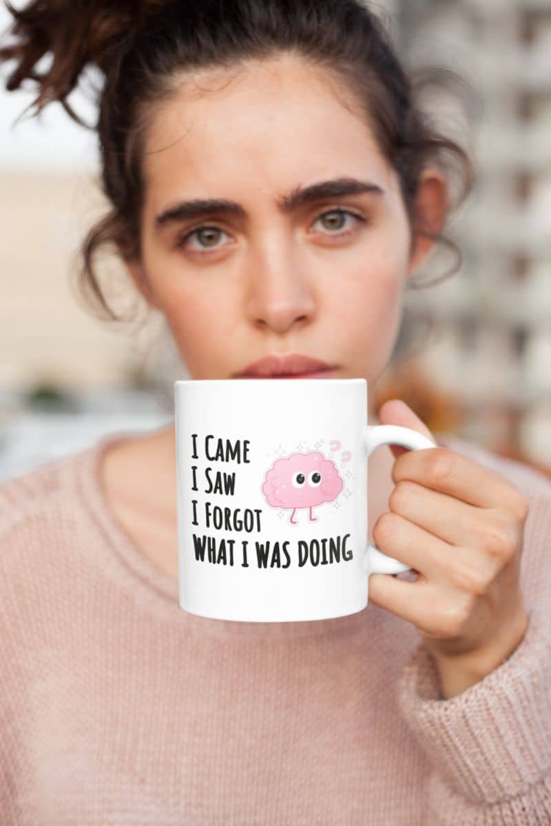 brain humor mug with a person holding a mug with a humorous design and text 'I came, I saw, I forgot what I was doing'.