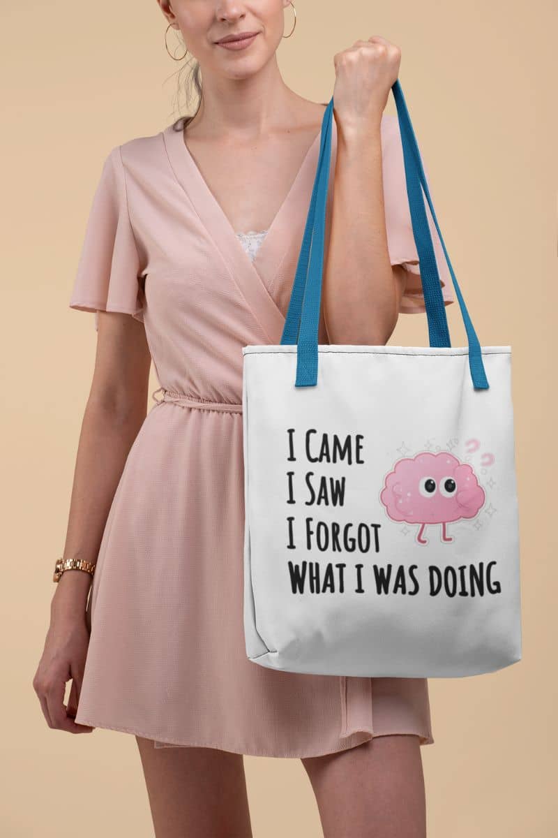 brain humor tote bag with a woman holding a tote bag with a humorous design and text 'I came, I saw, I forgot what I was doing'.
