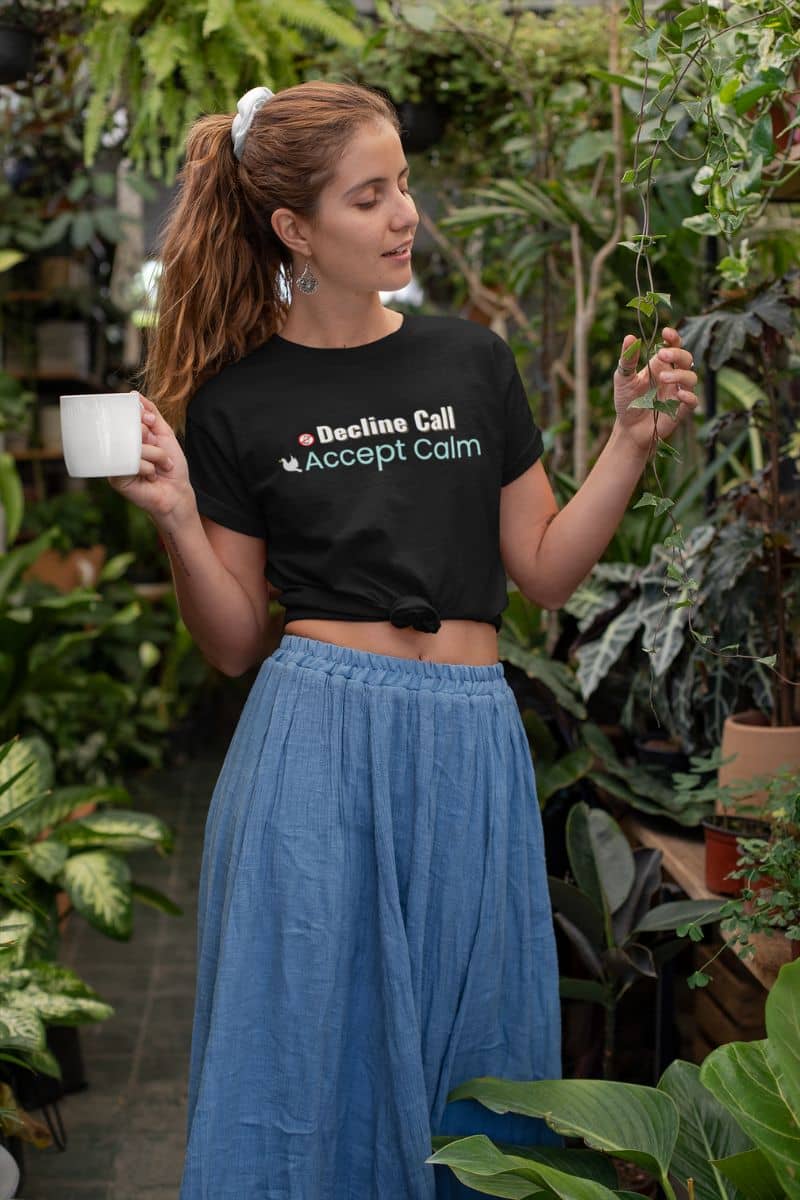 burnout recovery tee with a woman holding a cup and a plant in a garden setting, wearing a black t-shirt with text 'Decline Call, Accept Calm'.