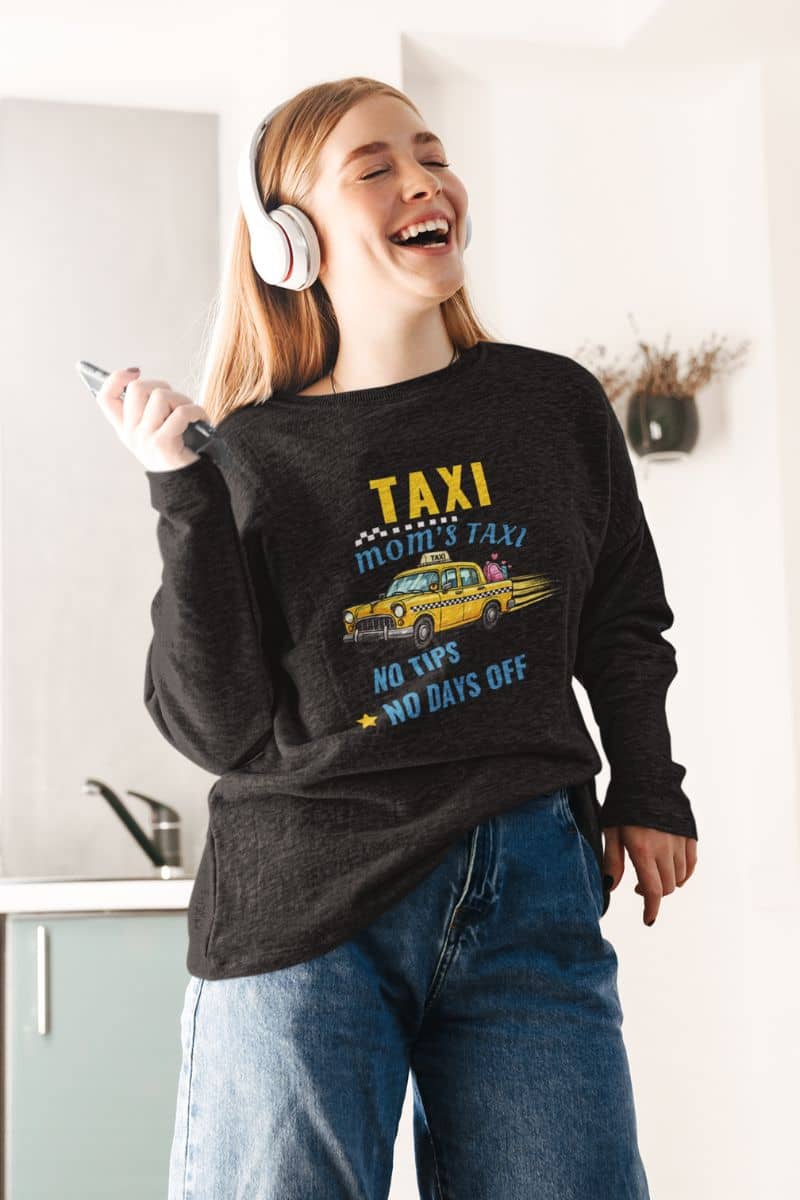 busy mom life sweatshirt with a person wearing a dark gray sweatshirt with a taxi graphic and text 'Taxi, Mom’s Taxi – No tips, no days off', standing in a kitchen.