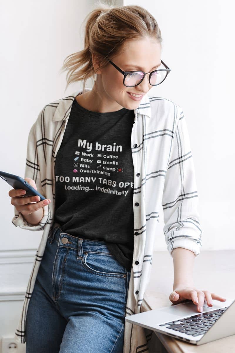 busy mind t shirt with a woman standing with her laptop, wearing a t-shirt featuring the text 'My Brain Has Too Many Tabs Open'