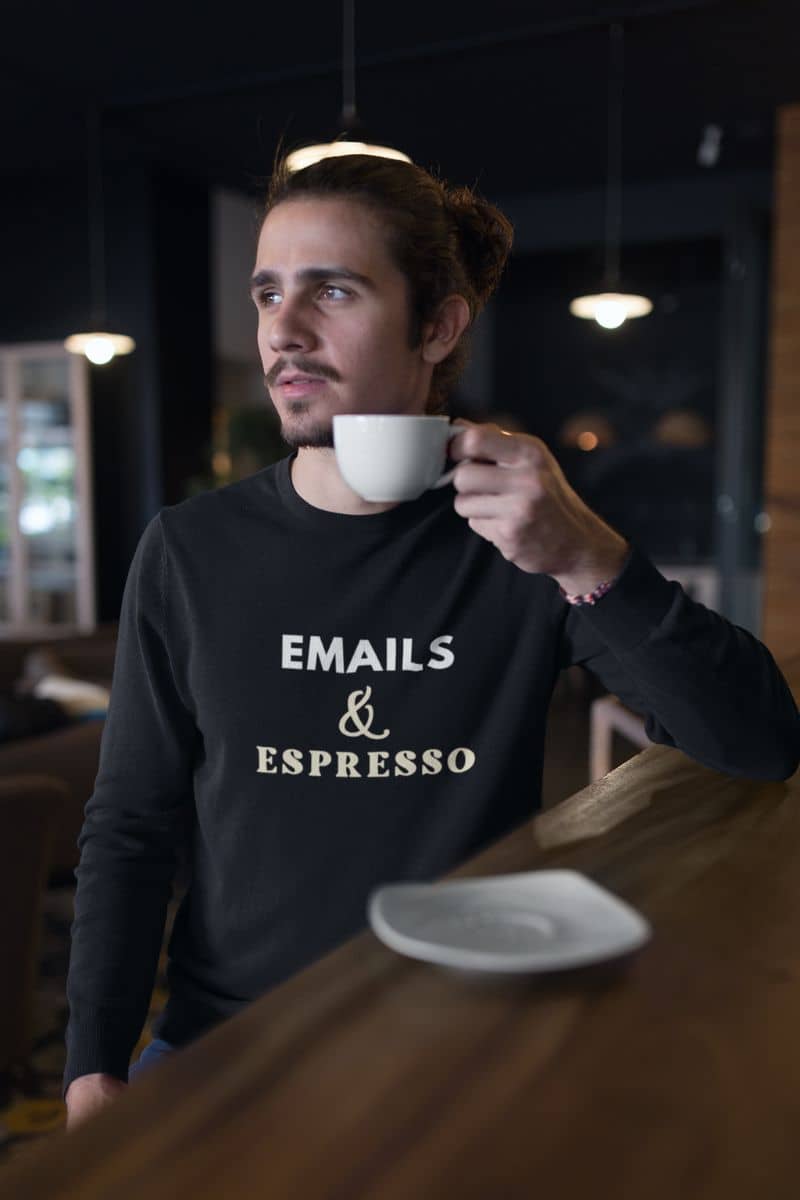 caffeine addict sweatshirt with a man holding a cup of coffee with 'EMAILS & ESPRESSO' text on a dark sweater in a cafe.