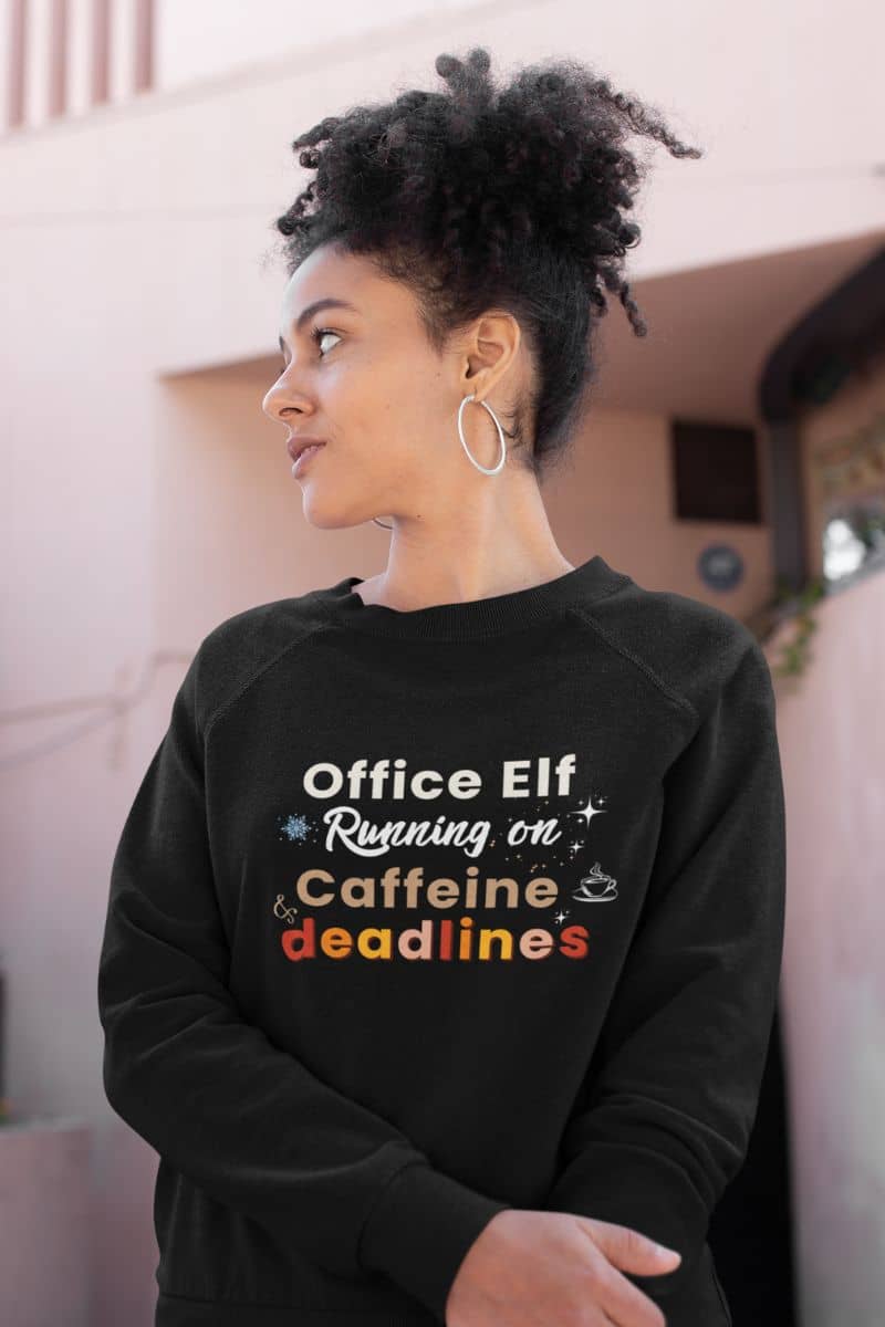 caffeine fueled sweatshirt with a person wearing a black sweatshirt with text 'Office Elf Running on Caffeine deadlines' in an indoor setting.