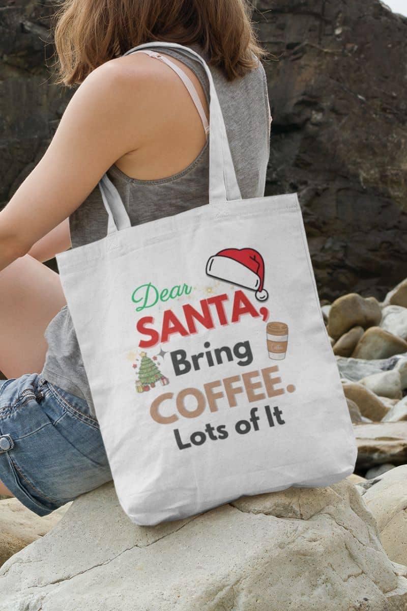 caffeine lover carryall with  a person holding a tote bag with text 'Dear Santa, Bring Coffee. Lots of It.' on a rocky surface