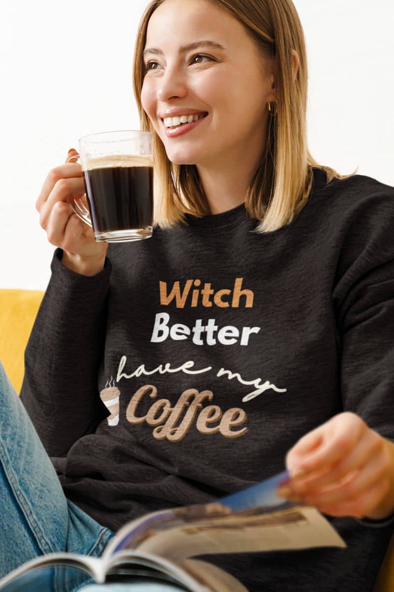 caffeine lover sweatshirt with a a woman wearing a black sweatshirt with text, holding a coffee cup and reading a magazine.