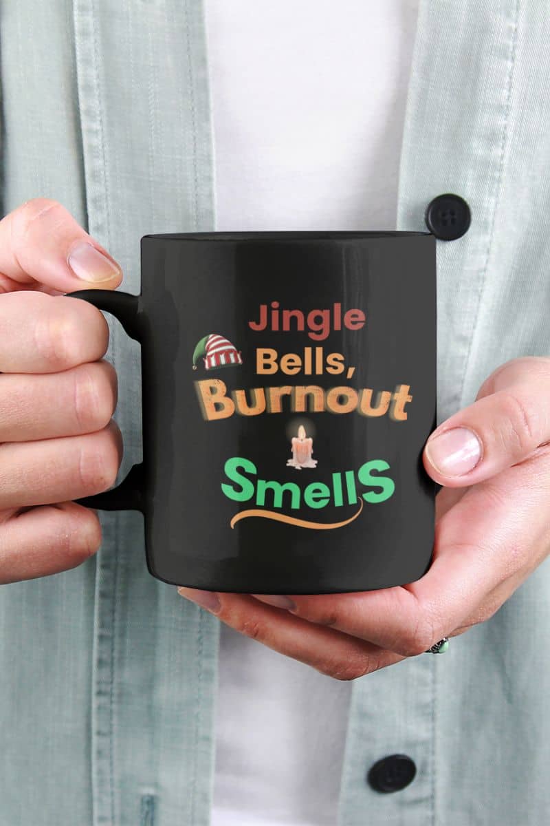 caffeine therapy mug with a person holding a black mug with humorous text 'Jingle Bells, Burnout Smells'