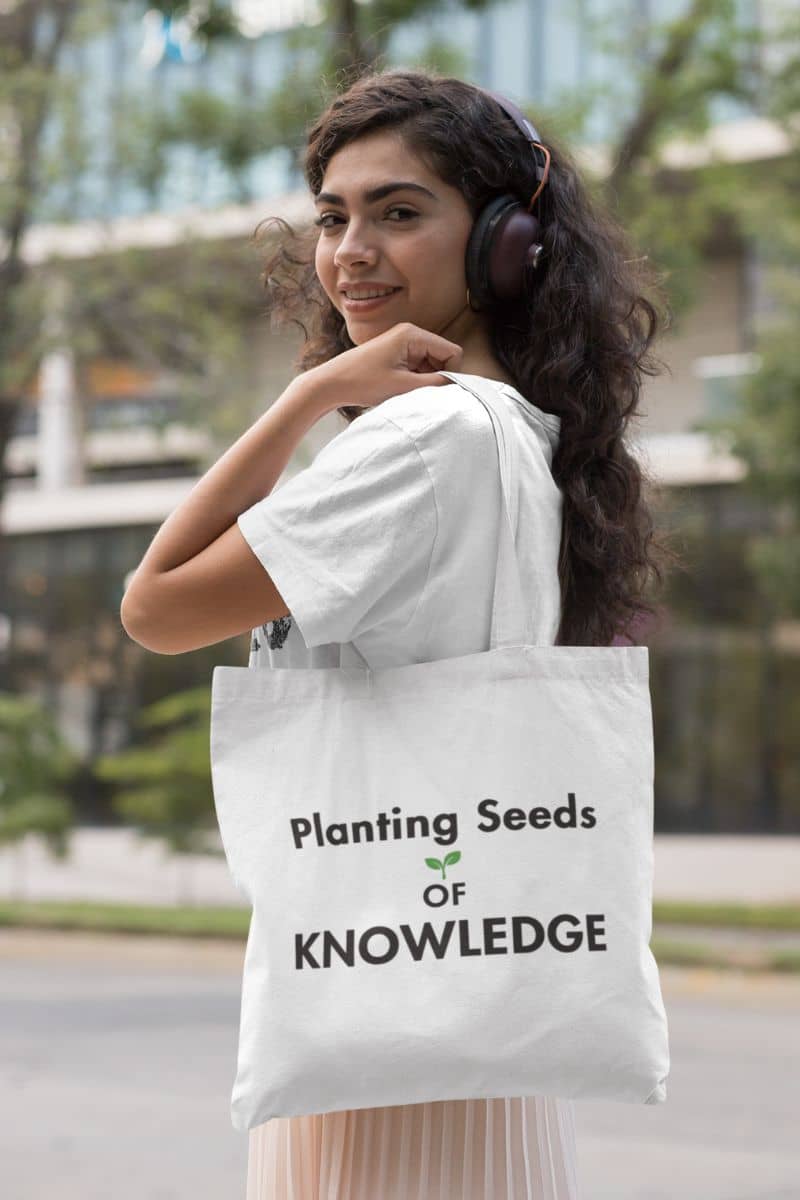 canvas teacher tote with a woman carrying a white tote bag featuring the text 'Planting Seeds OF KNOWLEDGE', wearing headphones and a white t-shirt 