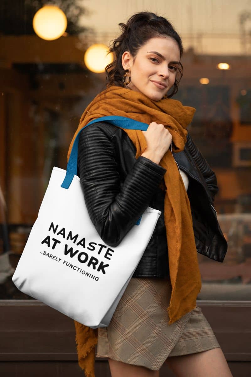 canvas work tote with a woman holding a tote bag with 'Namaste at Work...Rarely Functioning' text in an urban setting.