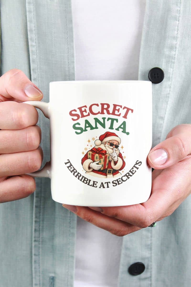 Ceramic Santa mugs featuring a retro Santa in sunglasses and a funny Christmas quote on a white mug held with both hands.