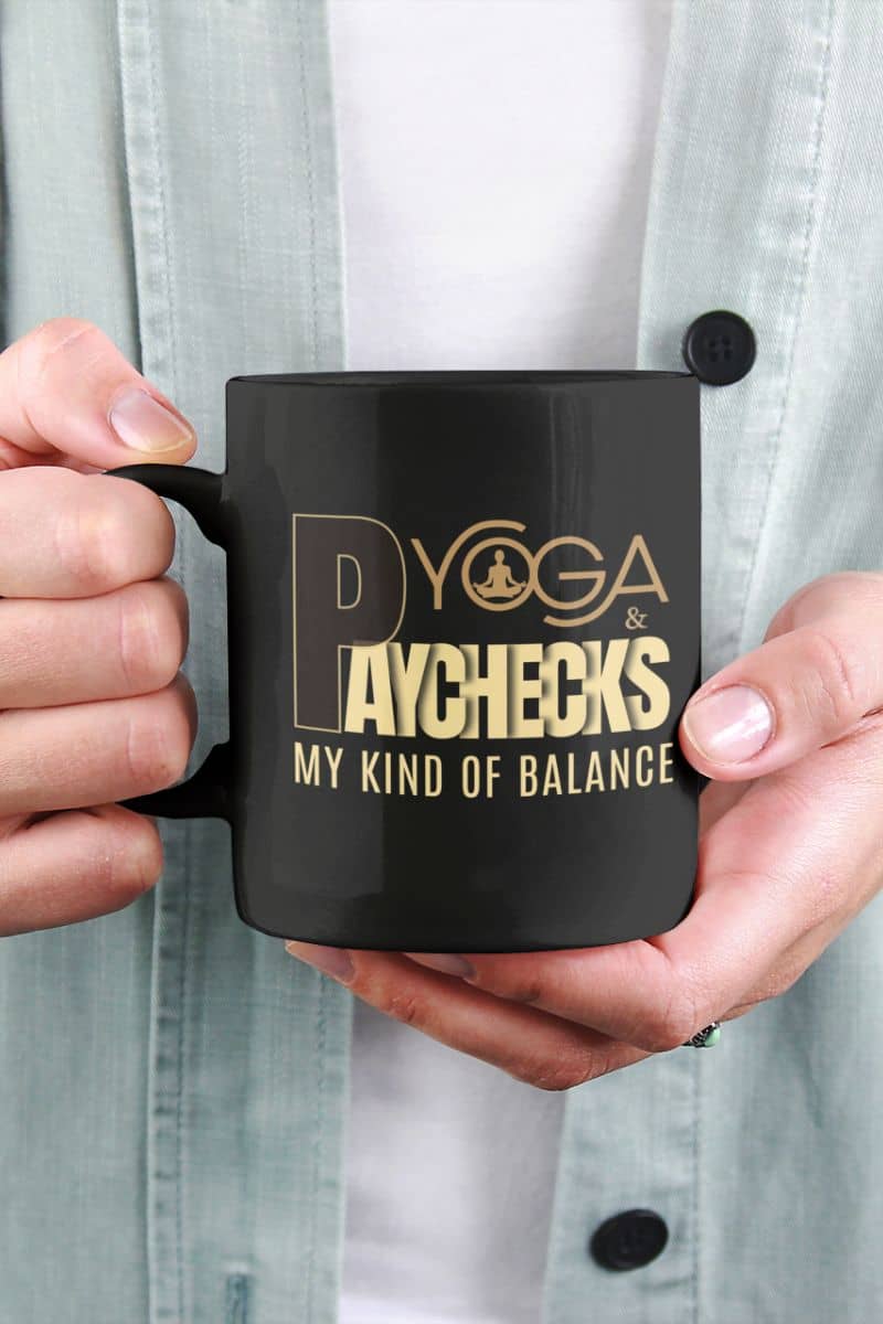 ceramic yoga mug with a person holding a black mug with gold text 'Yoga & Paychecks – My Kind of Balance'