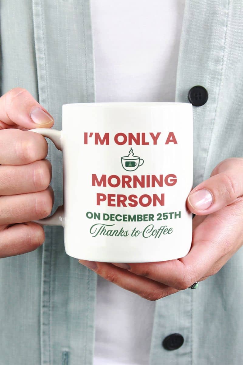 christmas caffeine mug with a person holding a mug with text 'I’m Only a Morning Person on December 25th', held by a person wearing a light gray shirt.