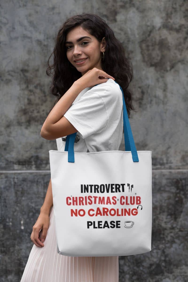 christmas humor bag with a woman holding a tote bag with text 'Introvert Christmas Club, No Caroling Please' against a gray wall.
