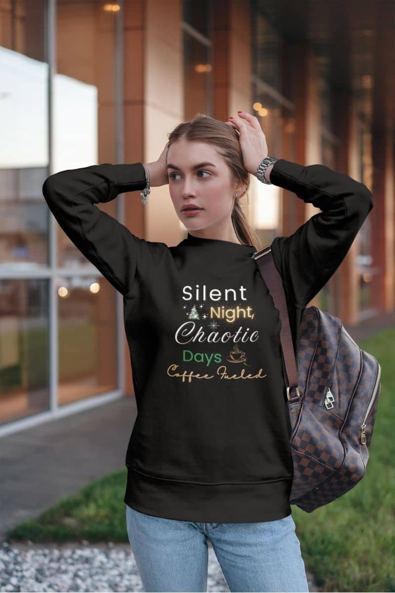 christmas humor pullover with a woman wearing a black sweatshirt with text 'Silent Night, Chaotic Days Coffee Fueled', standing outdoors.