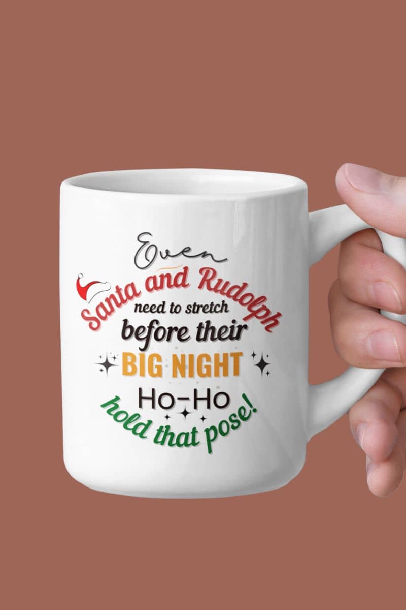 Christmas office coffee mug featuring a hand holding a mug with the text “Even Santa & Rudolph Need to Stretch Before Their Big Night. Ho-Ho-Hold That Pose!”